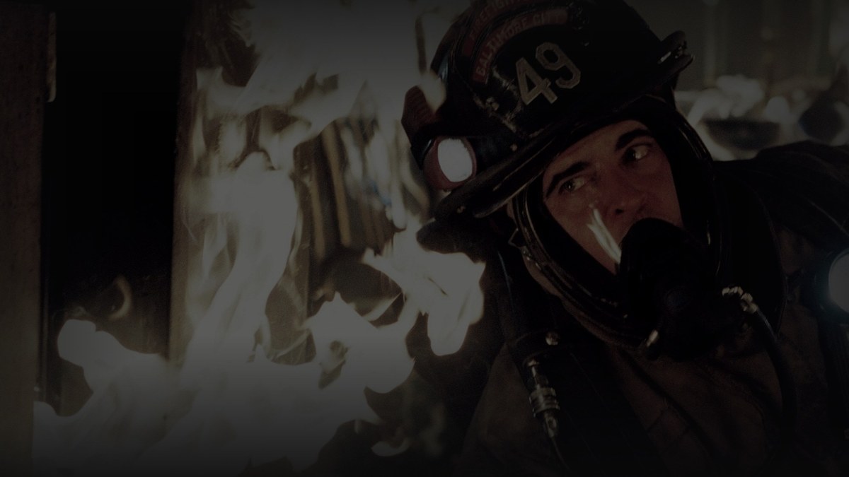 Still from Ladder 49 (2004) — tmdb backdrop (id 11128); genuine still of joaquin phoenix with helmet 49 and scba in flames. pre-darkened source to 0.72 (source luma 111.8) and baked through scripts/bake_dark_photo.py at factor 0.45, 1200x675, on-disk luma 28.1